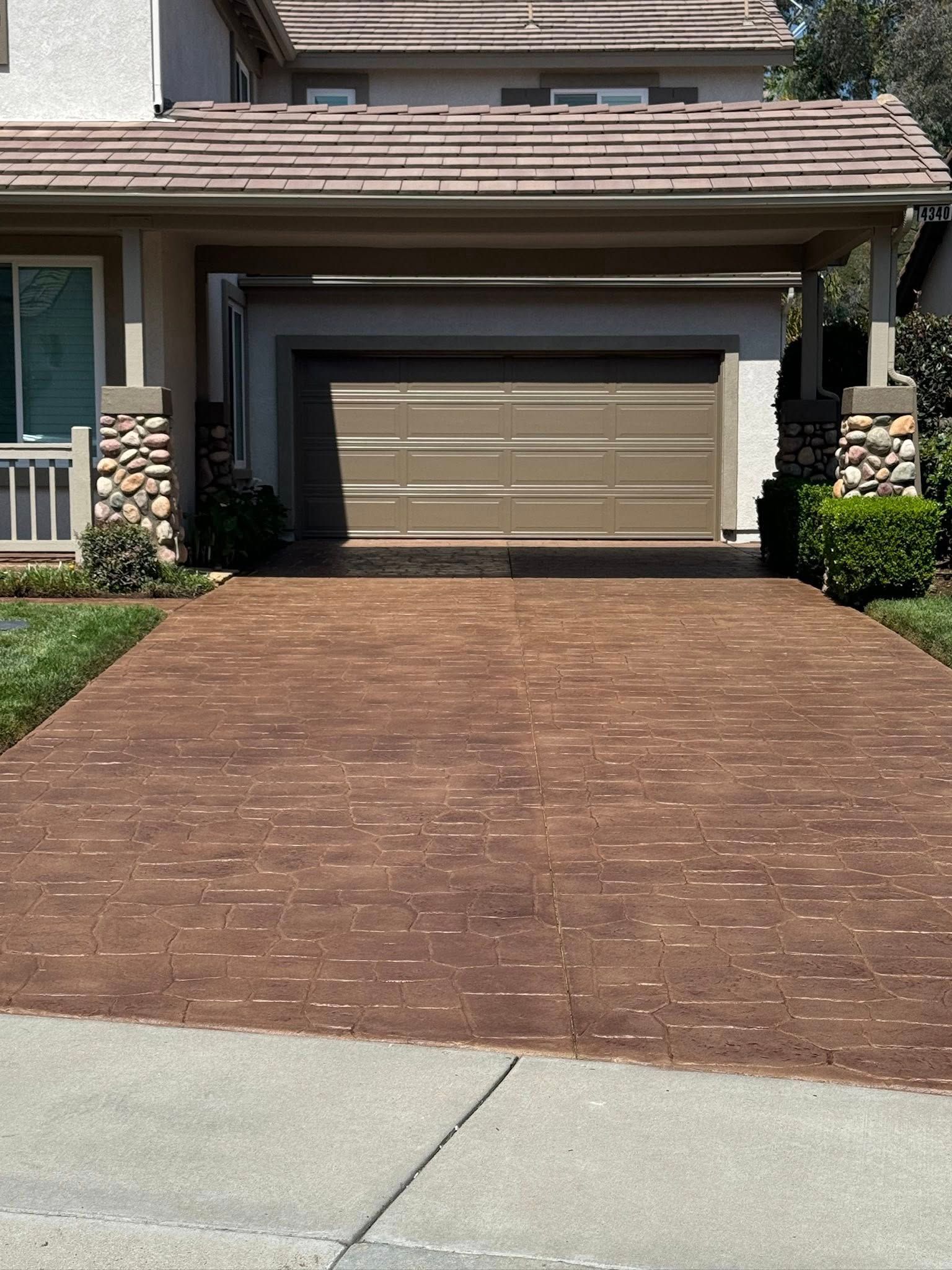 Brown brick driveway leading to a garage with a brown door. Columns with stone accents.
