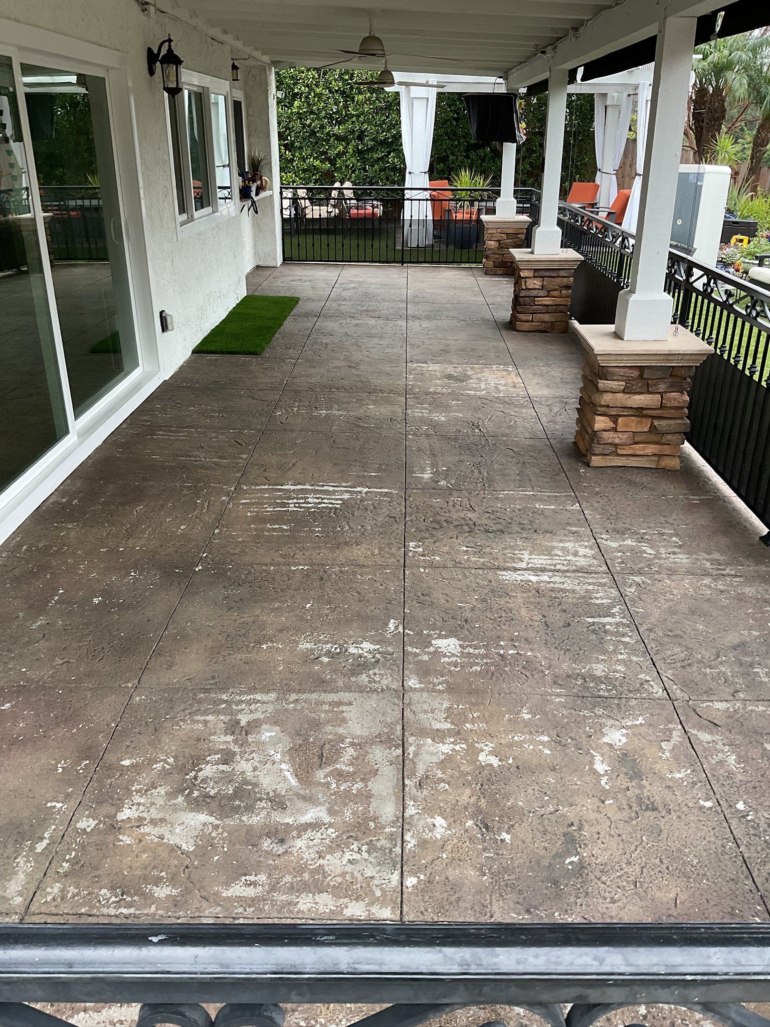 Concrete patio with peeling coating, black railing, and white columns.