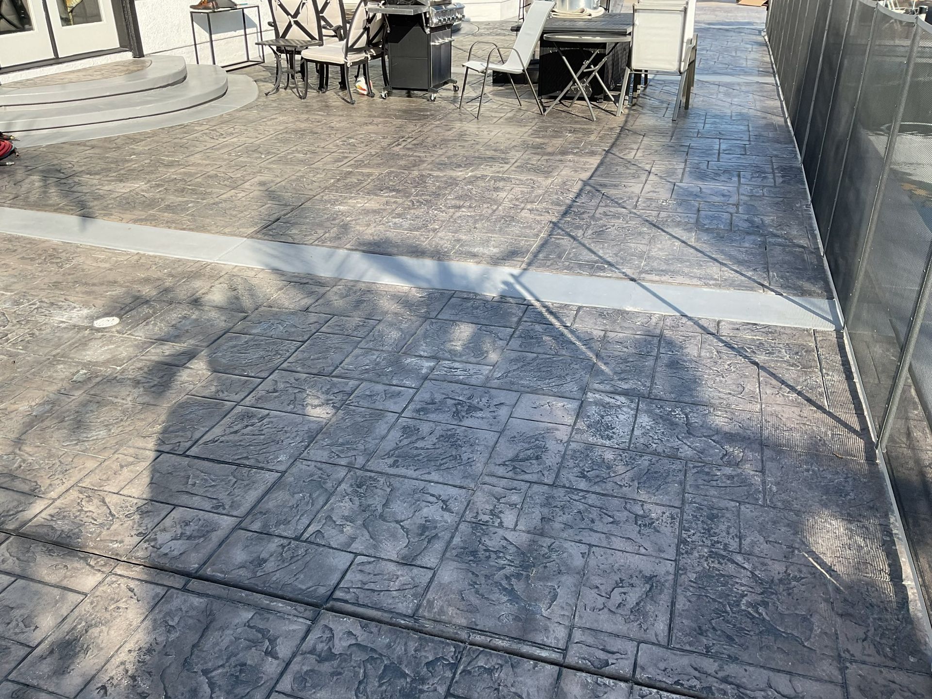 Stamped concrete patio, gray, with a raised seating area, and outdoor dining furniture.