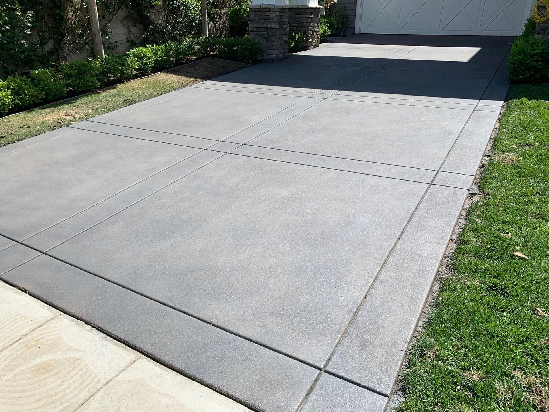 Concrete driveway with grid pattern, bordered by grass and sidewalk. Gray concrete.