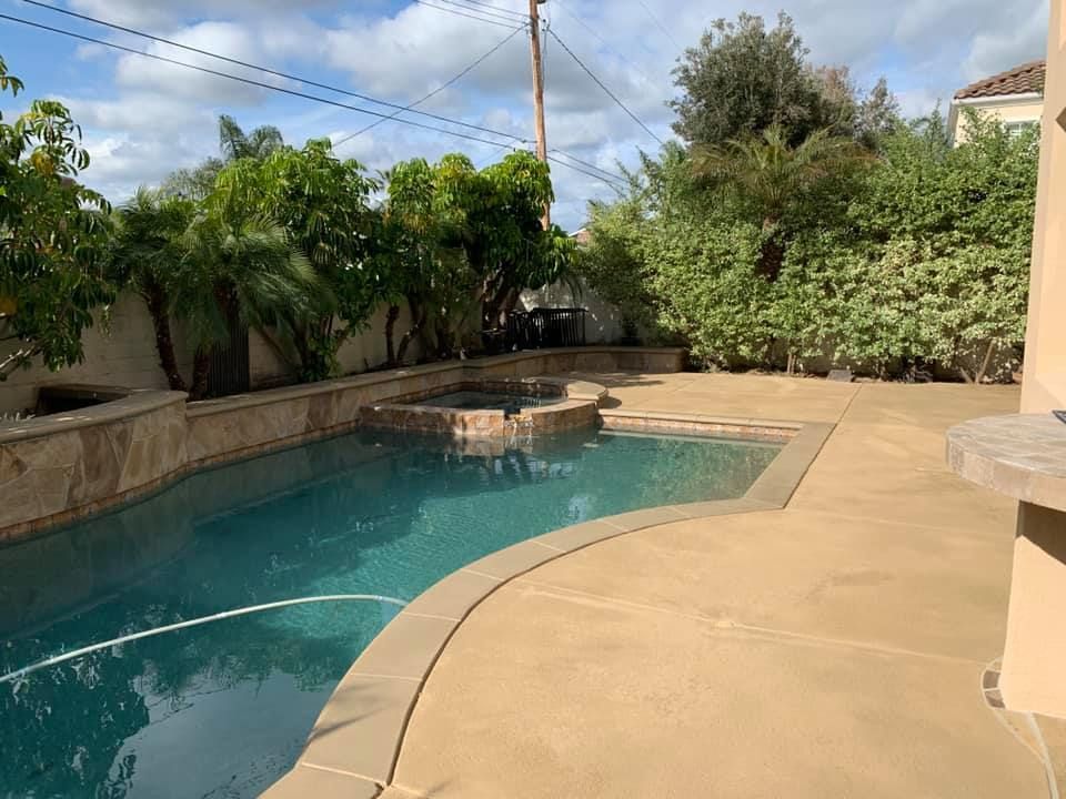 Backyard with pool and hot tub surrounded by trees and stone, on a sunny day.