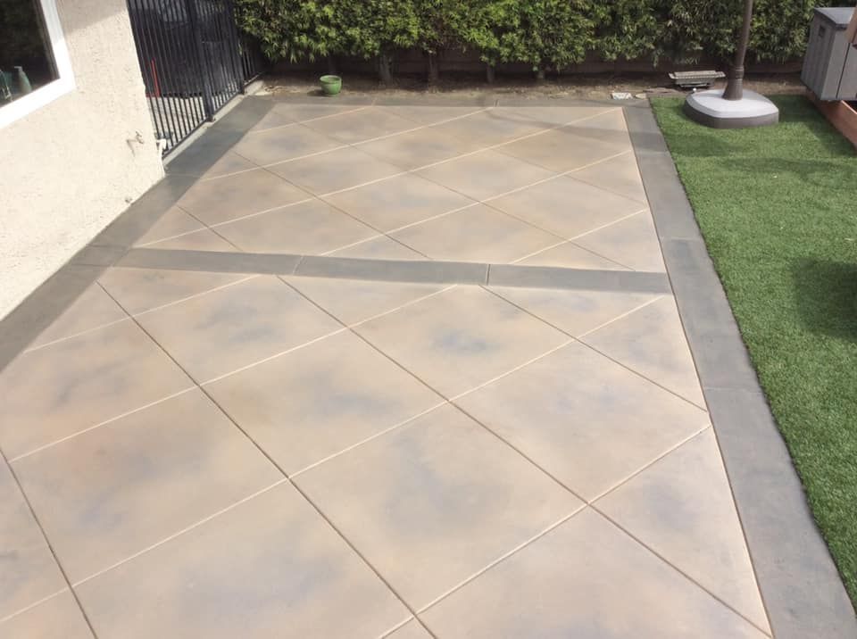 Concrete patio with a diagonal grid pattern, bordered by grass and a building.