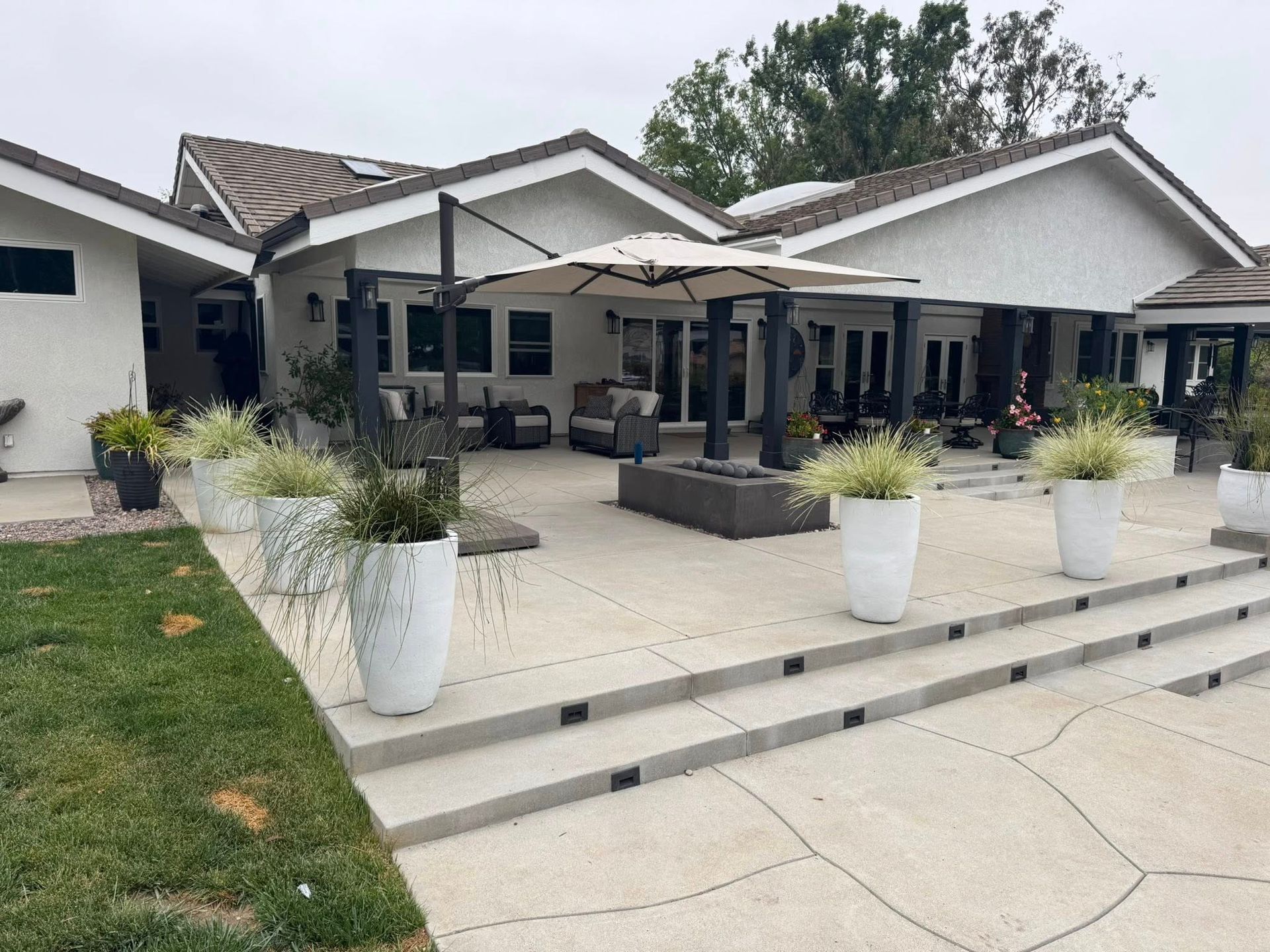 Backyard patio with white planters, gray concrete steps, and a white house.