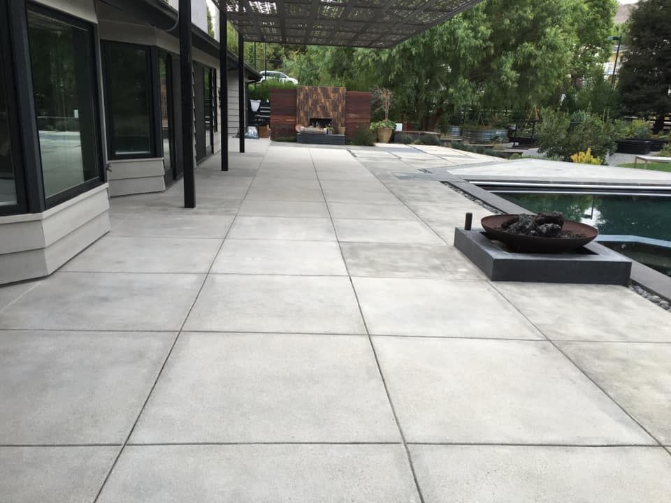 Concrete patio with dark lines, pool, fire pit, and building.