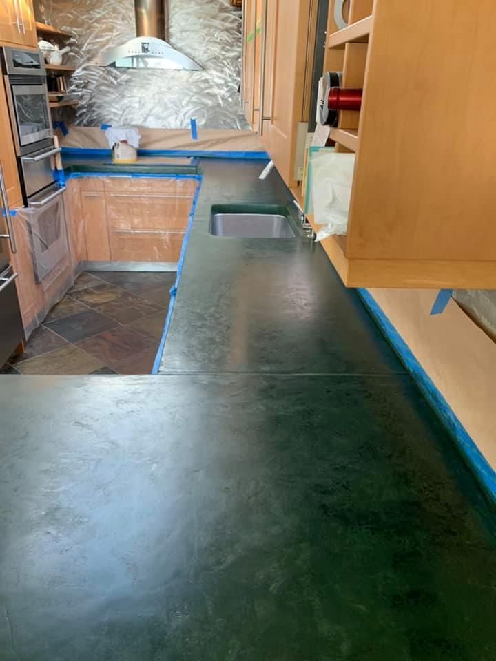 Kitchen with green countertops, wood cabinets, and appliances covered in blue tape for painting or remodeling.