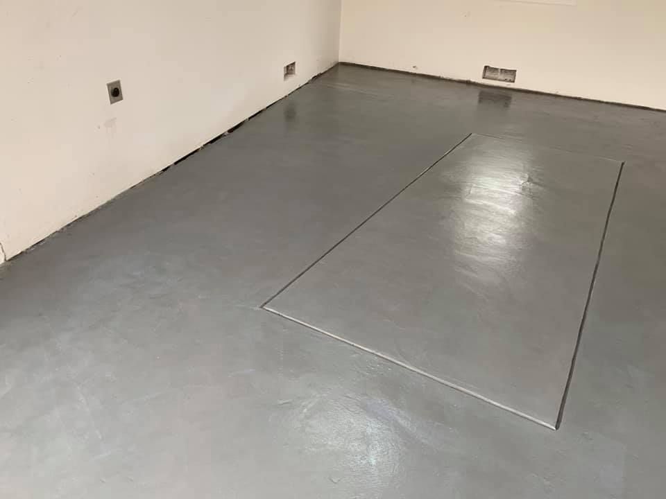 A room with a smooth gray epoxy floor, outlined rectangular area, and off-white walls.