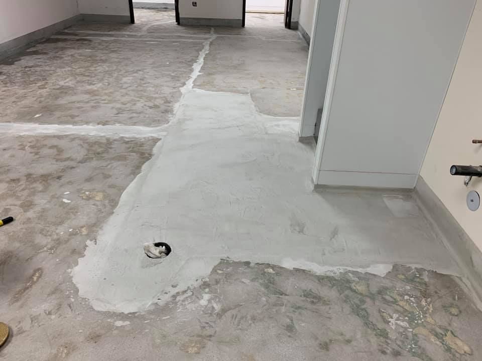 Concrete floor with grey patching, room with white walls, plumbing visible.