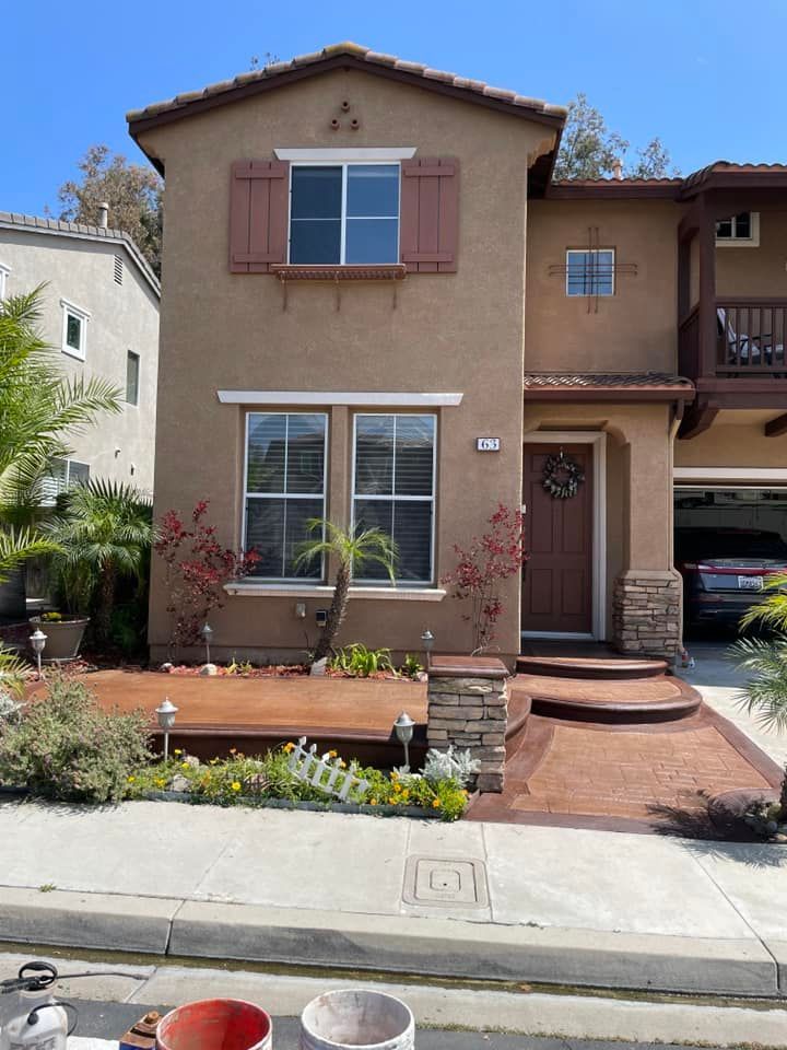 Two-story stucco house with brown trim, shutters, and door; a walkway and yard.