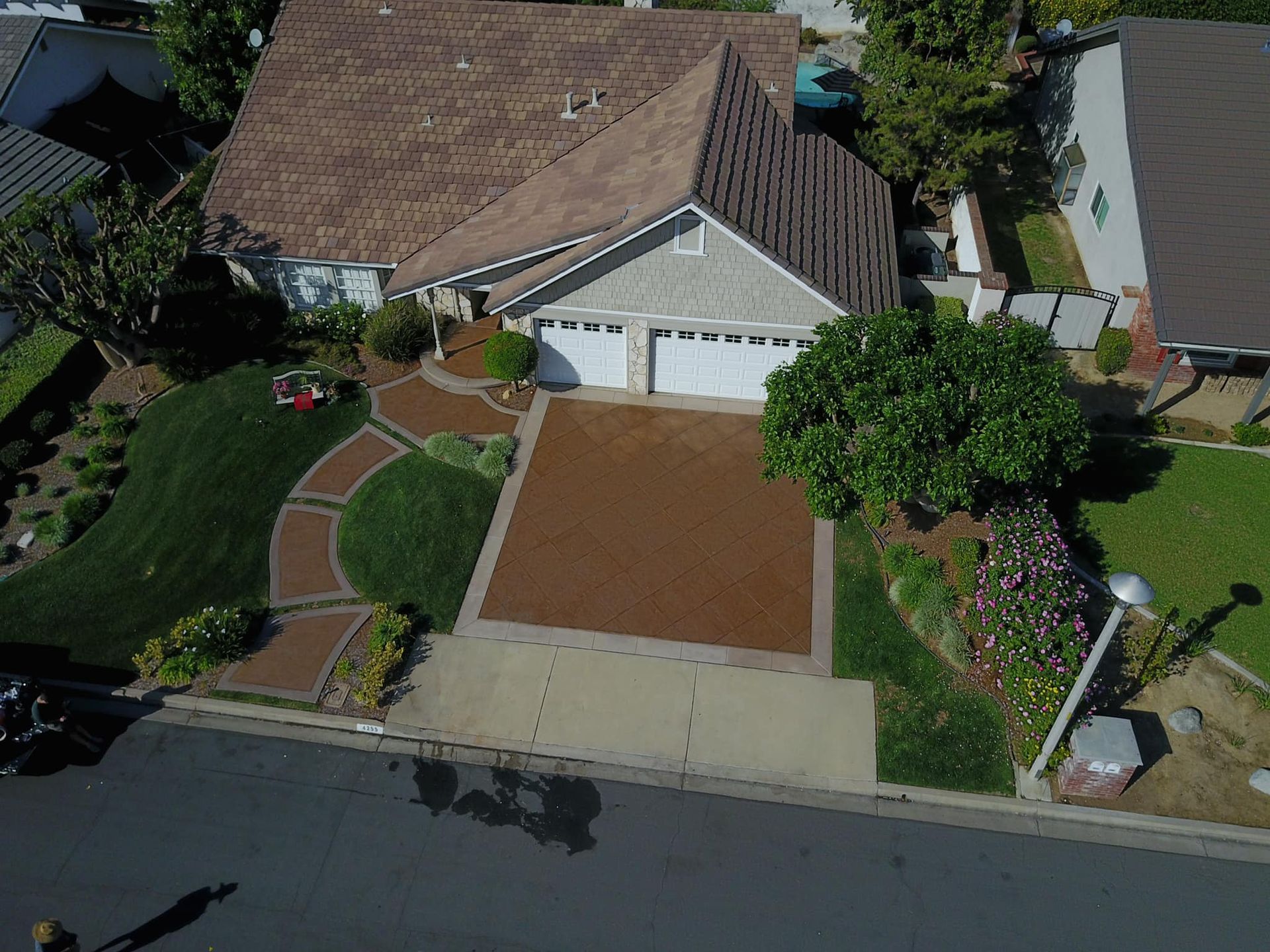 Aerial view of a house with a brown roof, white garage doors, and a landscaped front yard with brown mulch and green grass.