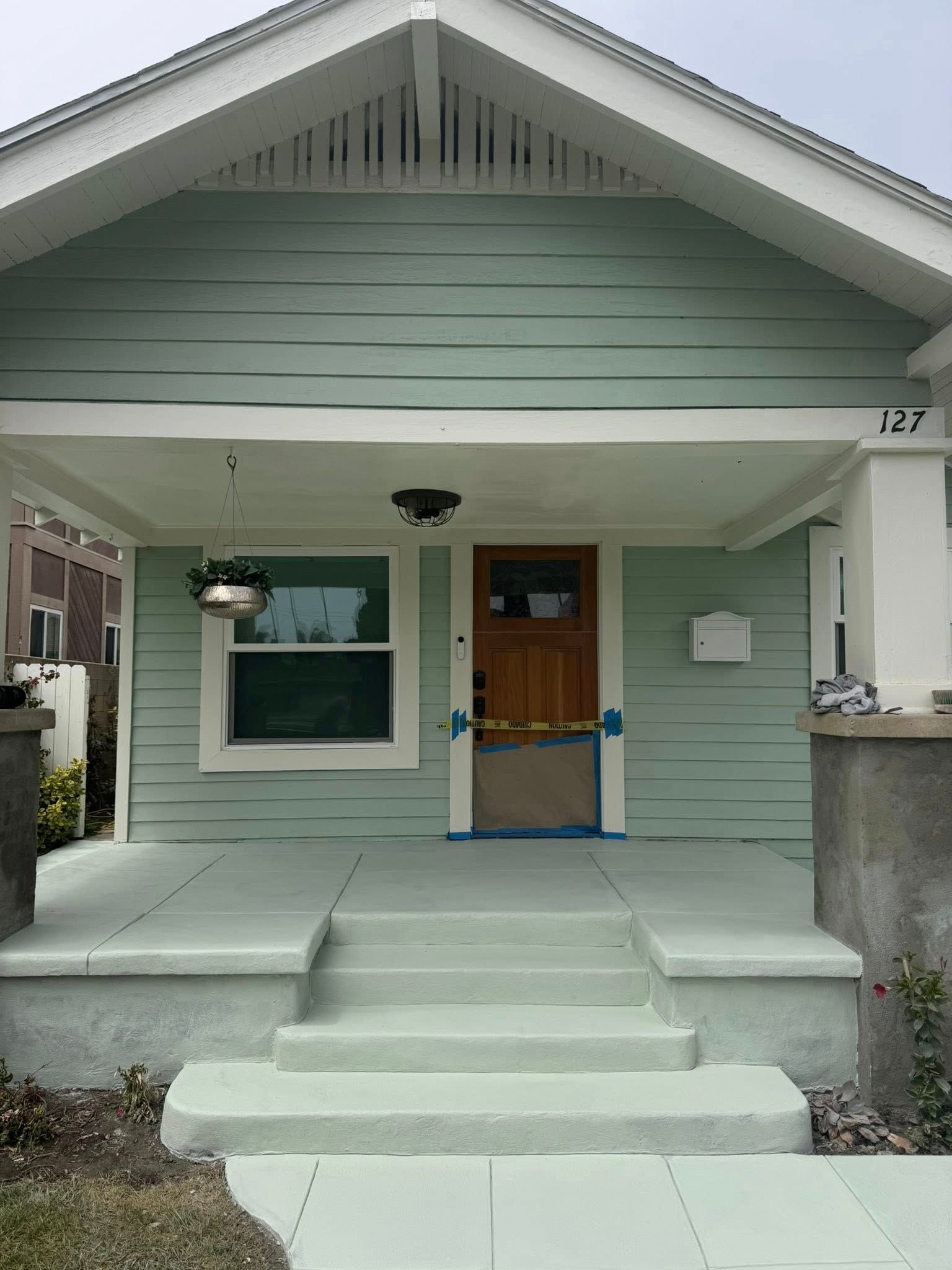 A light green house with a porch, steps, and a wooden door. House number 127.