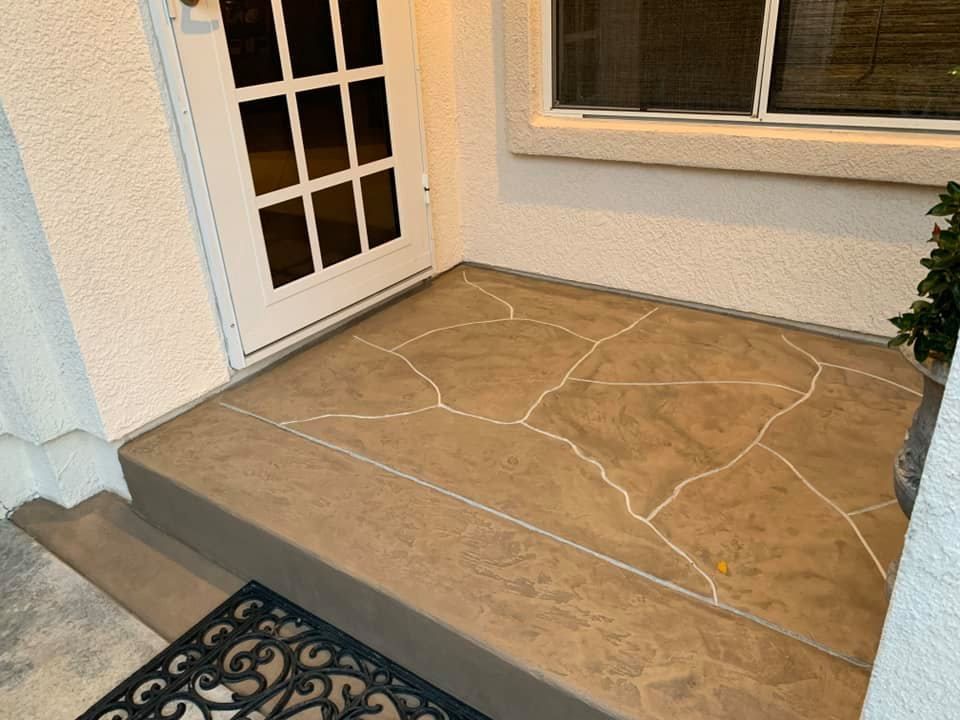 Brown concrete front porch with a patterned design, door, and window.