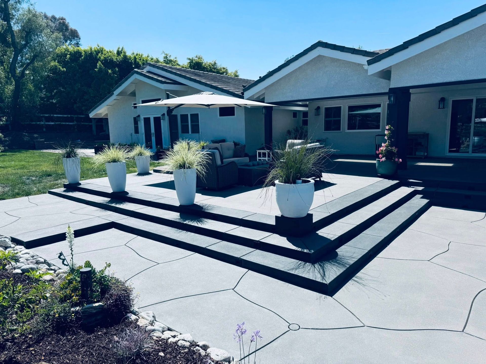 Patio with concrete steps and planters. White house with umbrella and seating.