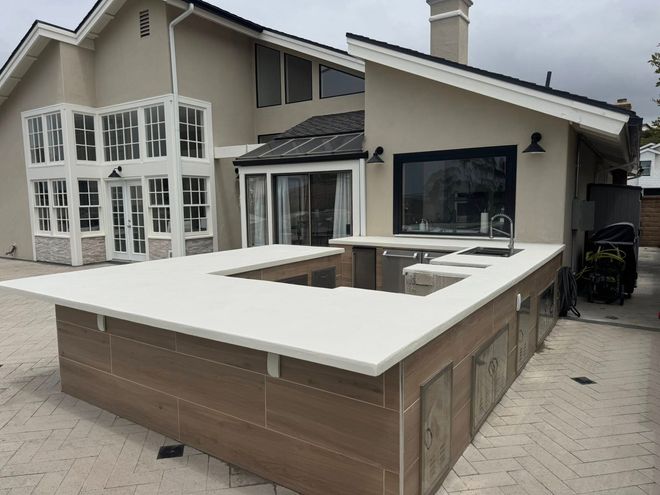 Outdoor kitchen with white countertop and wood paneling, set against a house.