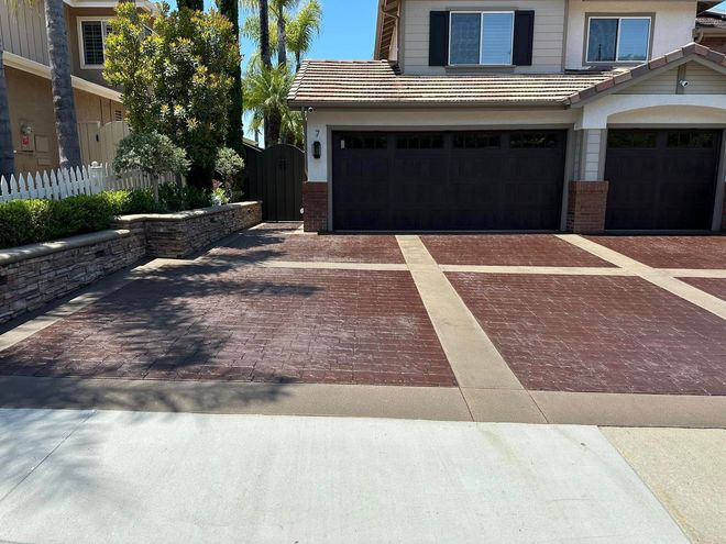 Driveway with red brick-like pattern. Two-car garage. Stone retaining wall and white picket fence.