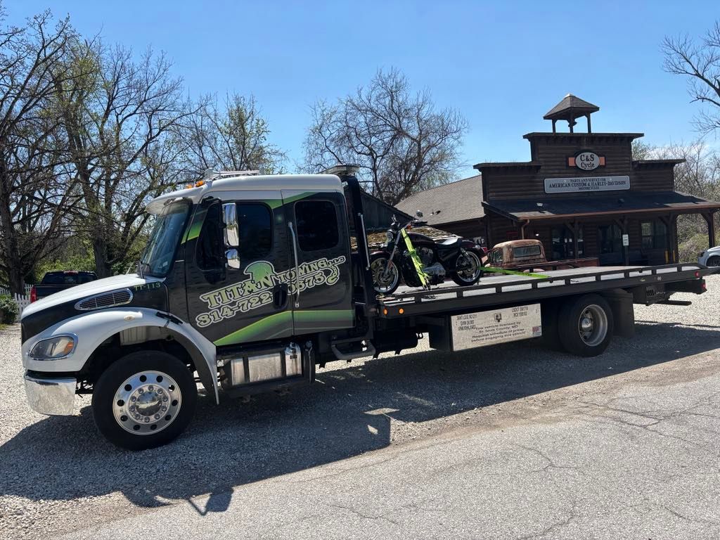 Tow truck with a motorcycle parked in front of a wooden Harley-Davidson building.
