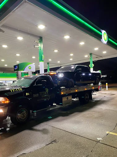 A black tow truck with a black pickup truck on its flatbed at a BP gas station at night.