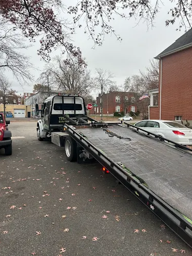 A tow truck with its ramp down in a residential area, preparing to load a vehicle. Leaves are scattered on the ground.