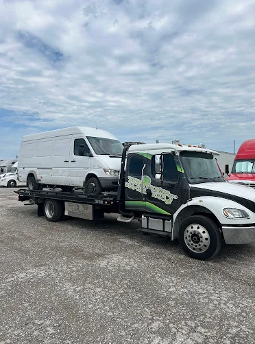 A white van is loaded onto a flatbed tow truck under a partly cloudy sky. The truck is white and green.