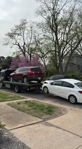 A red SUV is being towed onto a flatbed truck on a residential street. A white sedan is parked nearby.