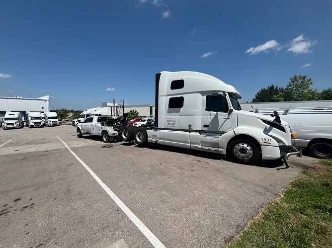 A white semi-truck with front-end damage next to a damaged white pickup truck on a sunny, paved lot.