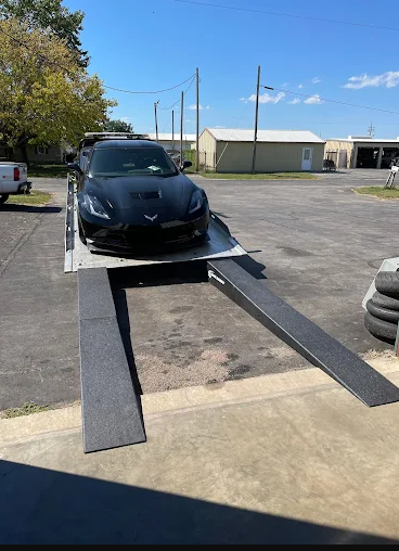 Black Corvette on a car lift, ready for service at an auto shop, under a clear blue sky.