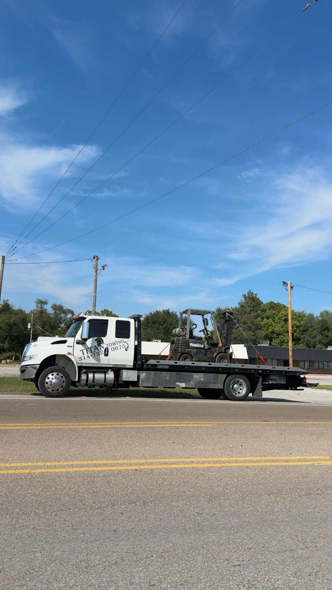 White tow truck on a road under a blue sky with trees.