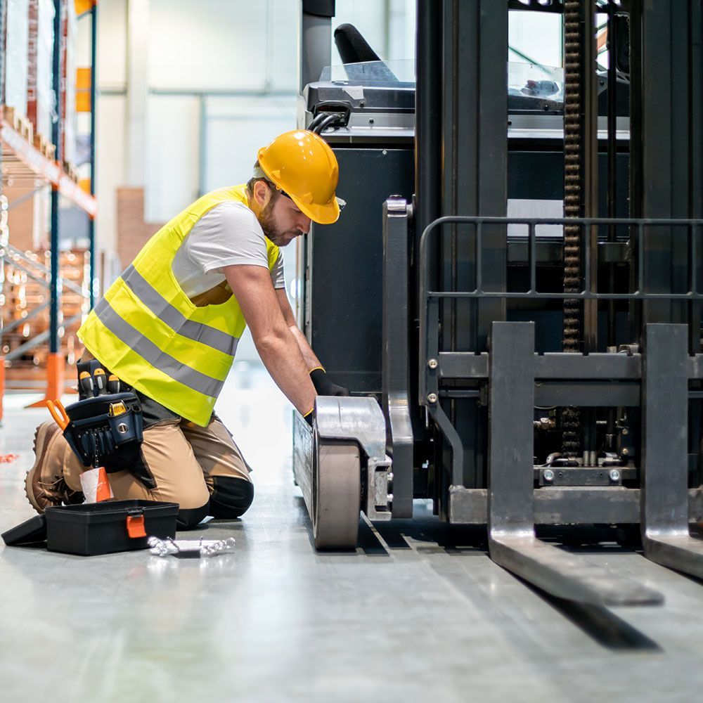 A man is working on a forklift in a warehouse.