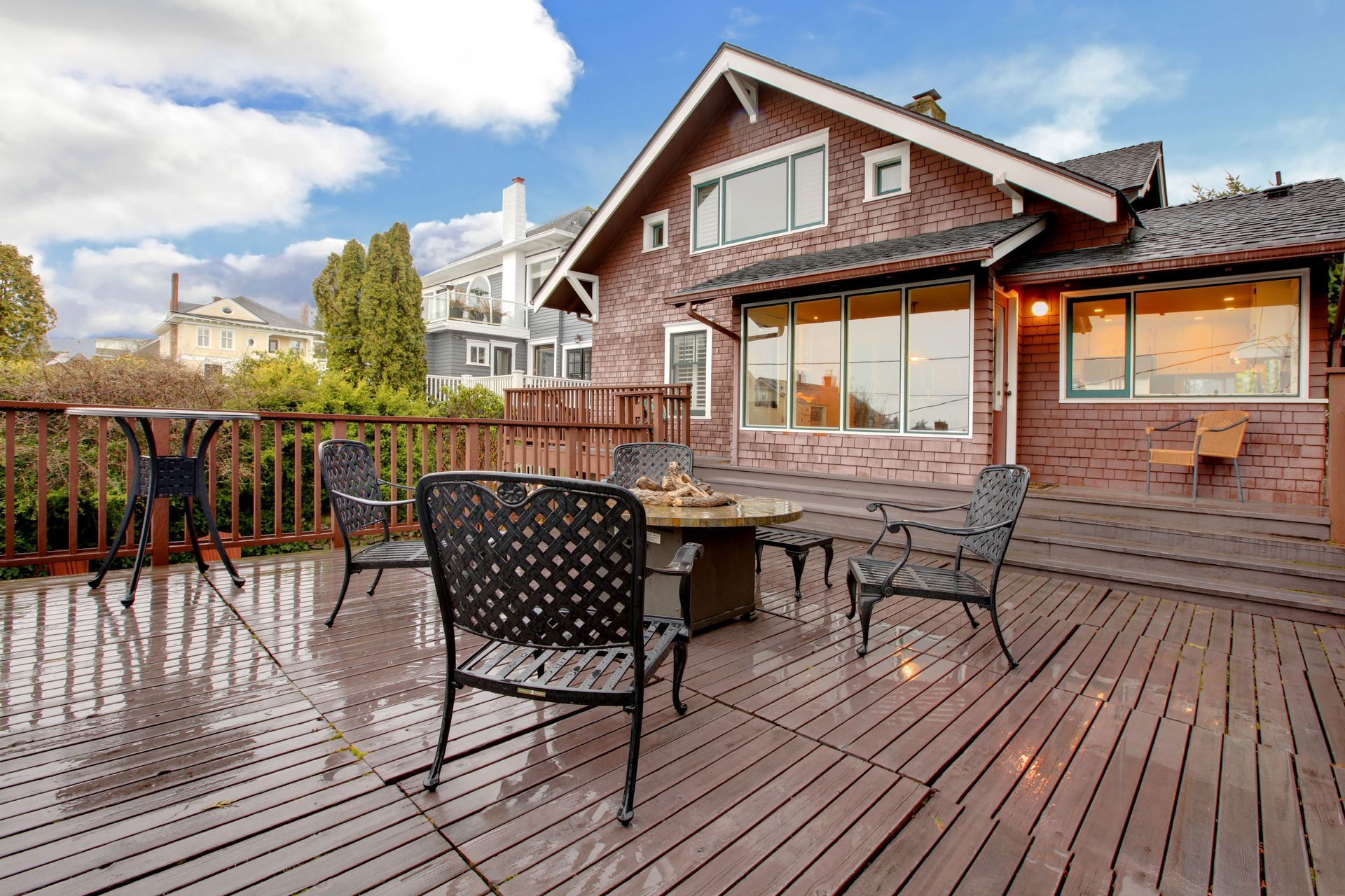 Wooden deck with patio chairs beside a brick house under a cloudy sky