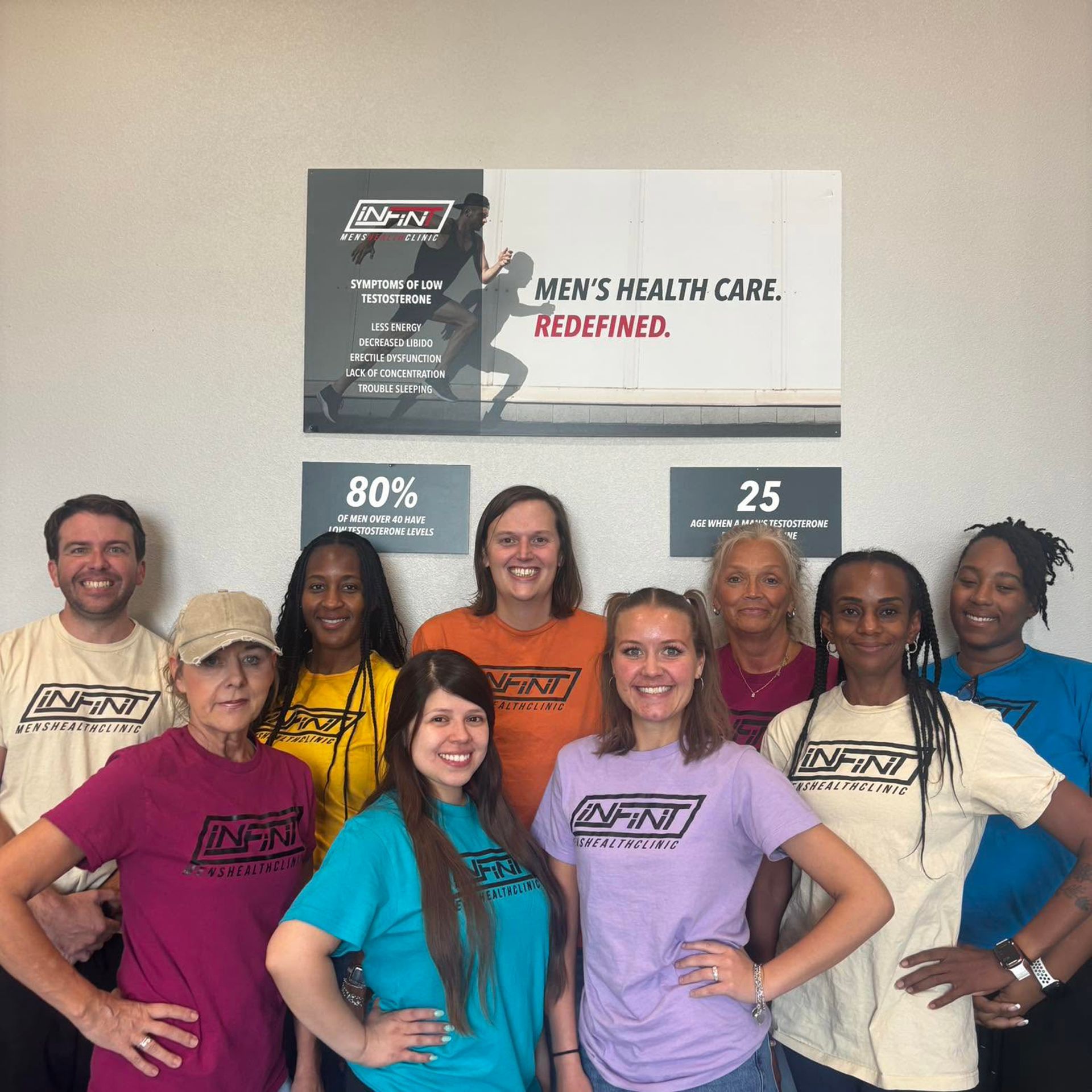 Group of smiling people posing indoors in front of a health care sign and poster.