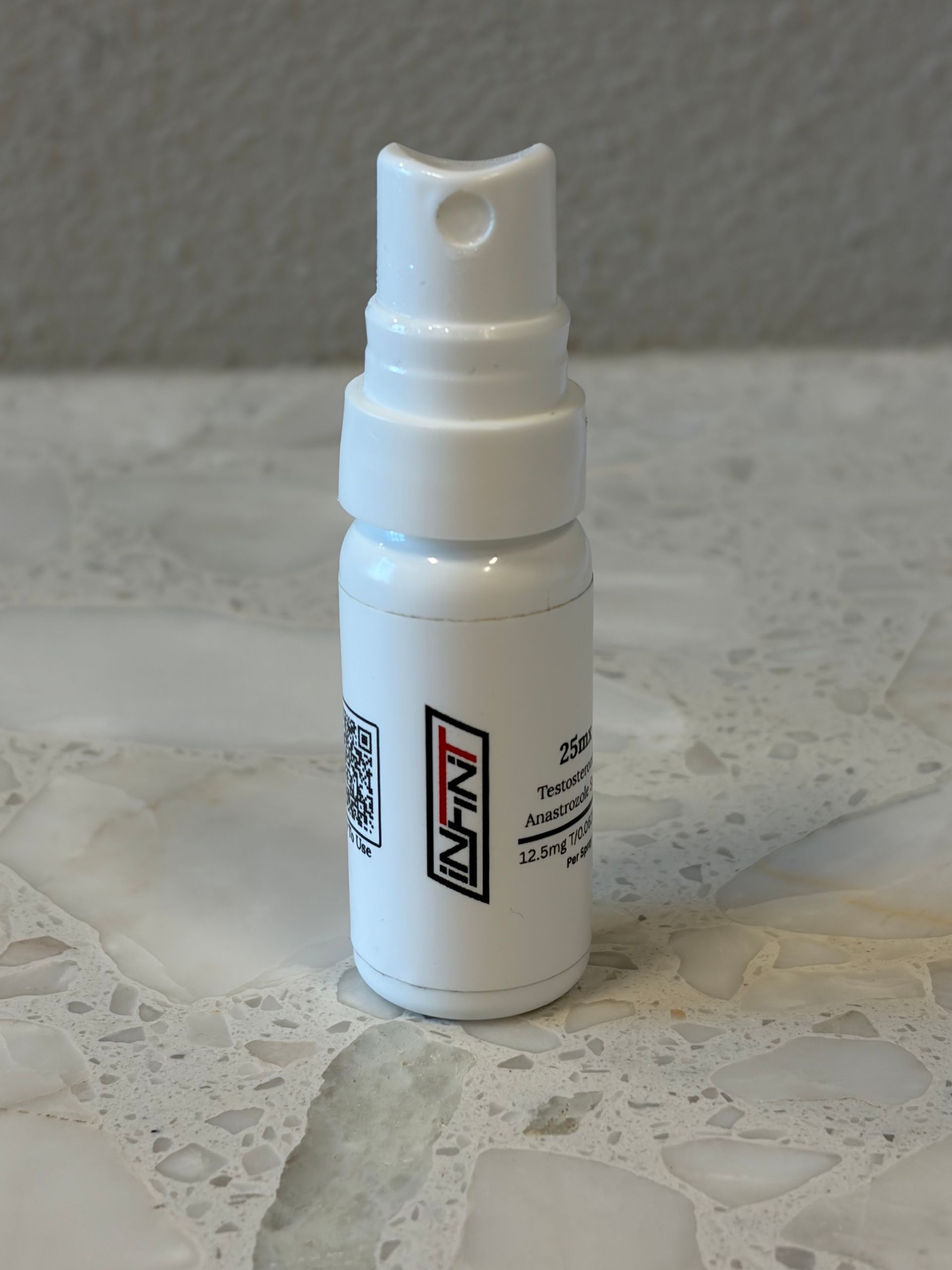 Small white spray bottle with a nozzle on a light stone surface.