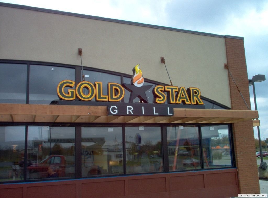 Gold Star Grill sign above large windows. Beige building with black star and flame logo.