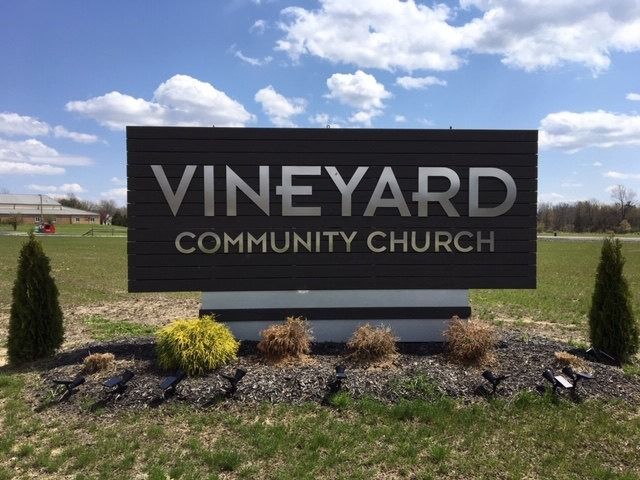 Sign for Vineyard Community Church with dark background, silver lettering, and landscaping.