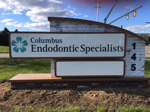 Sign for Columbus Endodontic Specialists with logo and address 145, set in front of a grassy area with a blue sky.