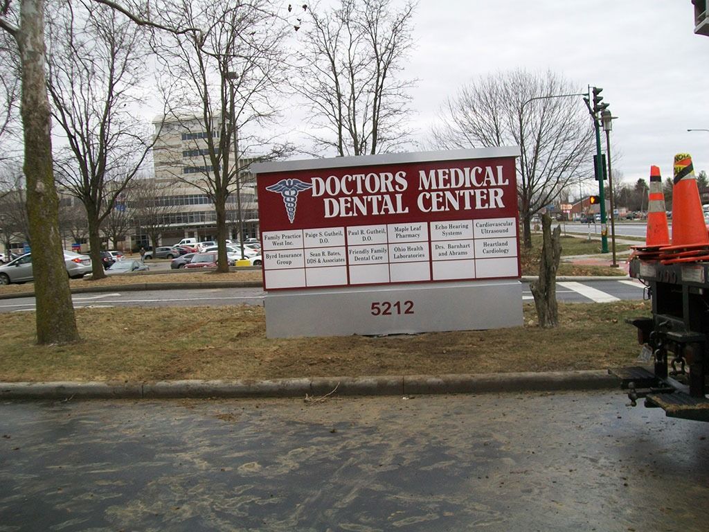 Doctors Medical Dental Center sign at 5212, with a building and parked cars in the background.