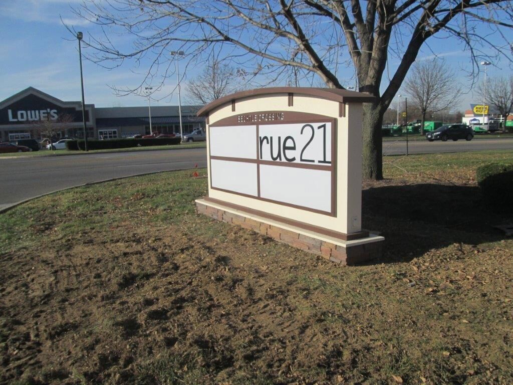 Sign for rue21 store with Lowe's in the background on a brown grassy area.