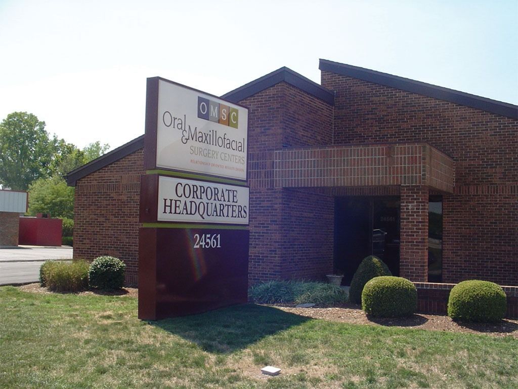 Sign for OakWood Homes and Curfence Headquarters in front of a brick building; green lawn.