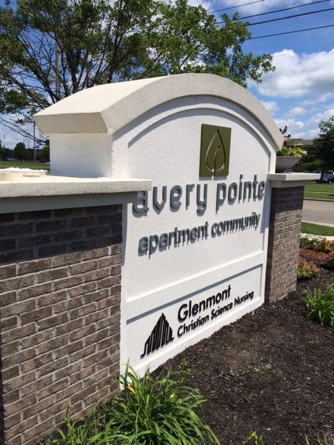 Sign for Avery Pointe apartment community, white with brick base, green logo, Glenmont Christian Science Nursing.