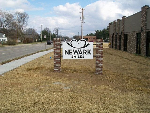 Sign for Newark Smiles dental office with brick columns, next to a street.