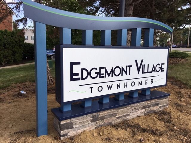 Sign for Edgemont Village Townhomes: Blue and white sign with dark base and green grass.