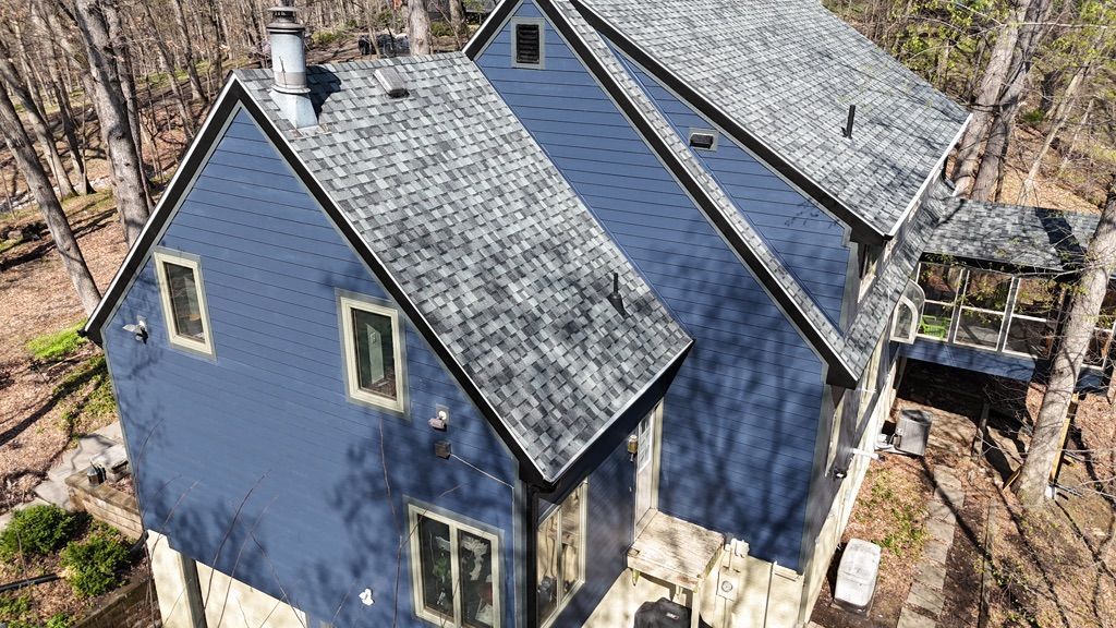 An aerial view of a blue house with a gray roof surrounded by trees.