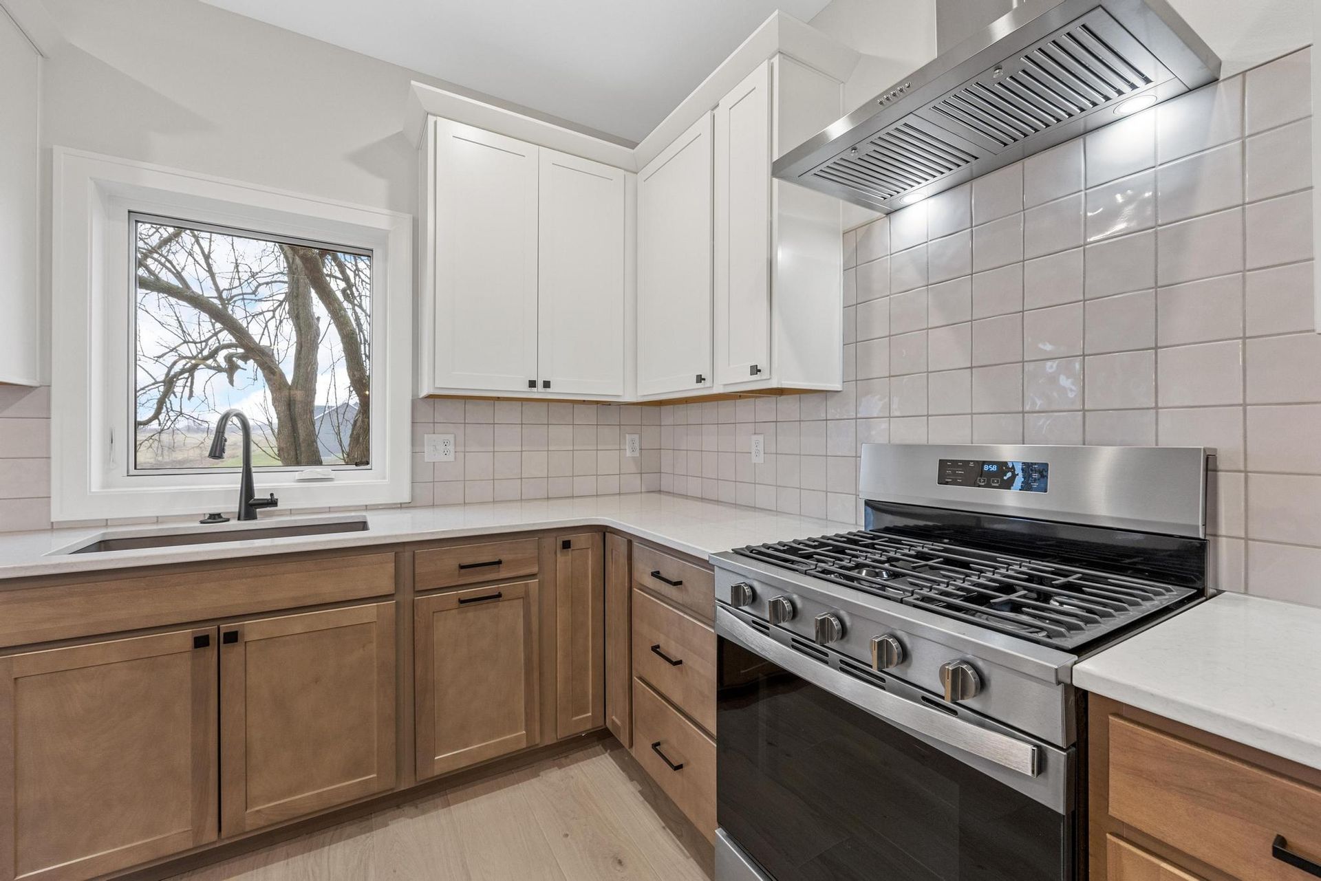A kitchen with wooden cabinets , a stove , a sink , and a window.