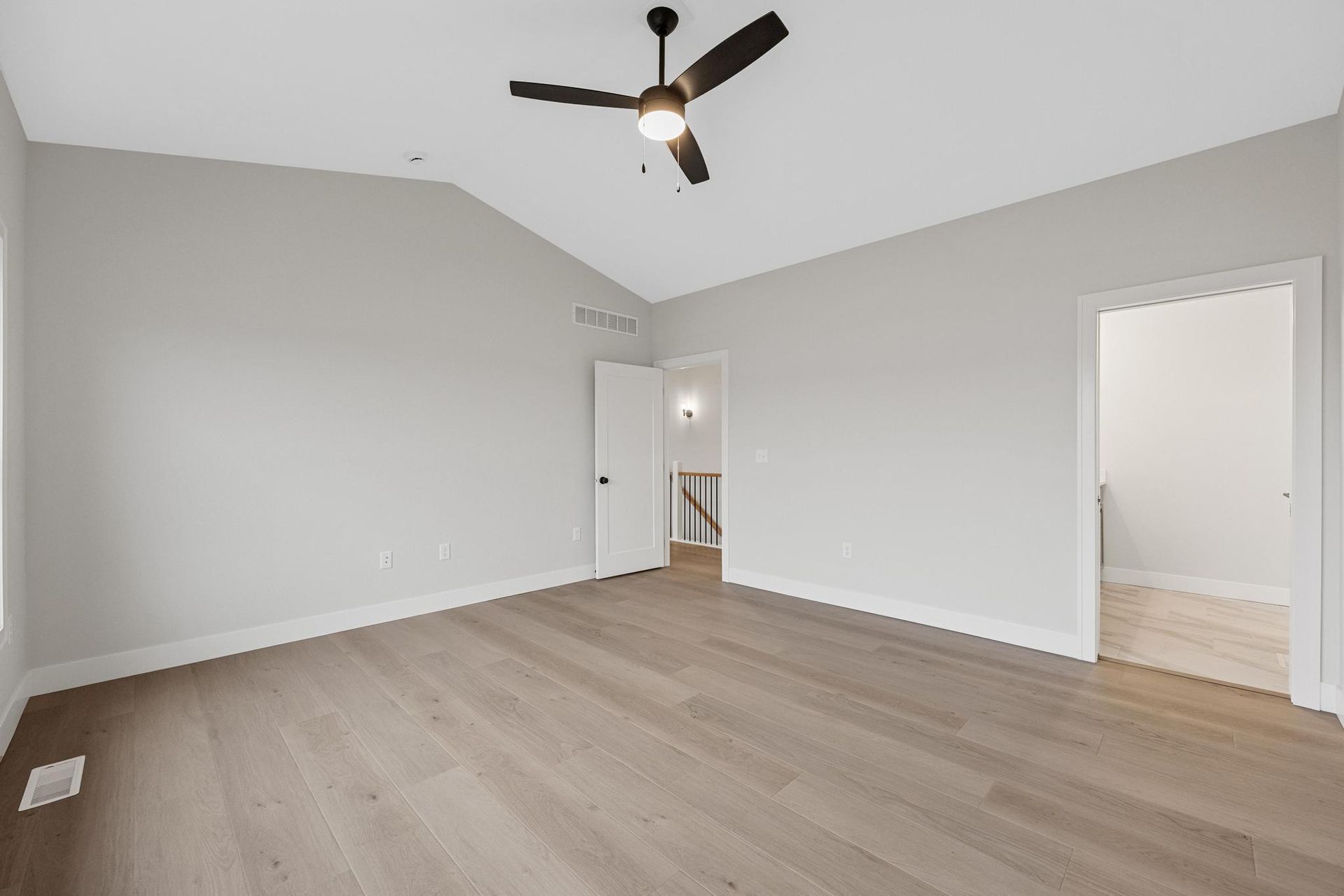 An empty bedroom with hardwood floors and a ceiling fan.