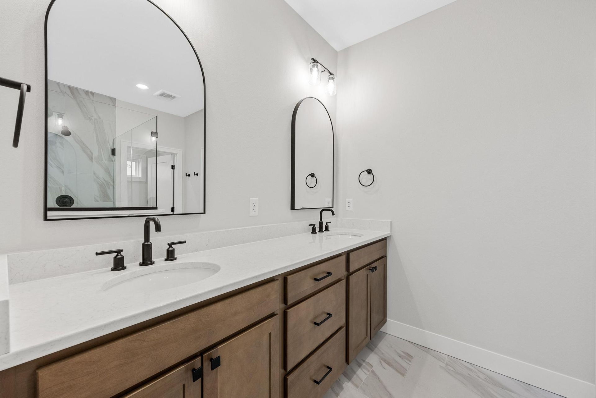 A bathroom with two sinks , two mirrors , and a walk in shower.