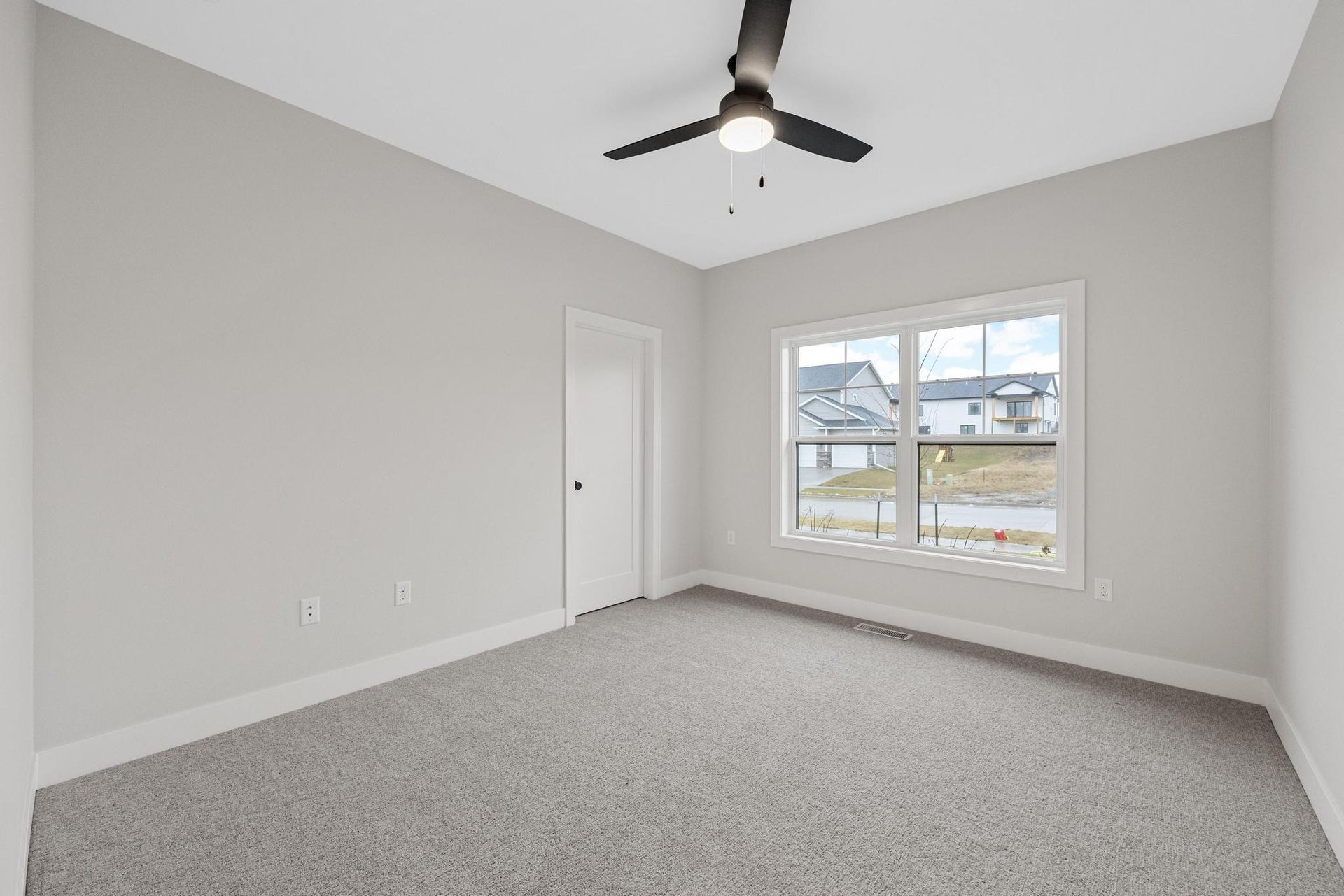 An empty bedroom with a ceiling fan and two windows.