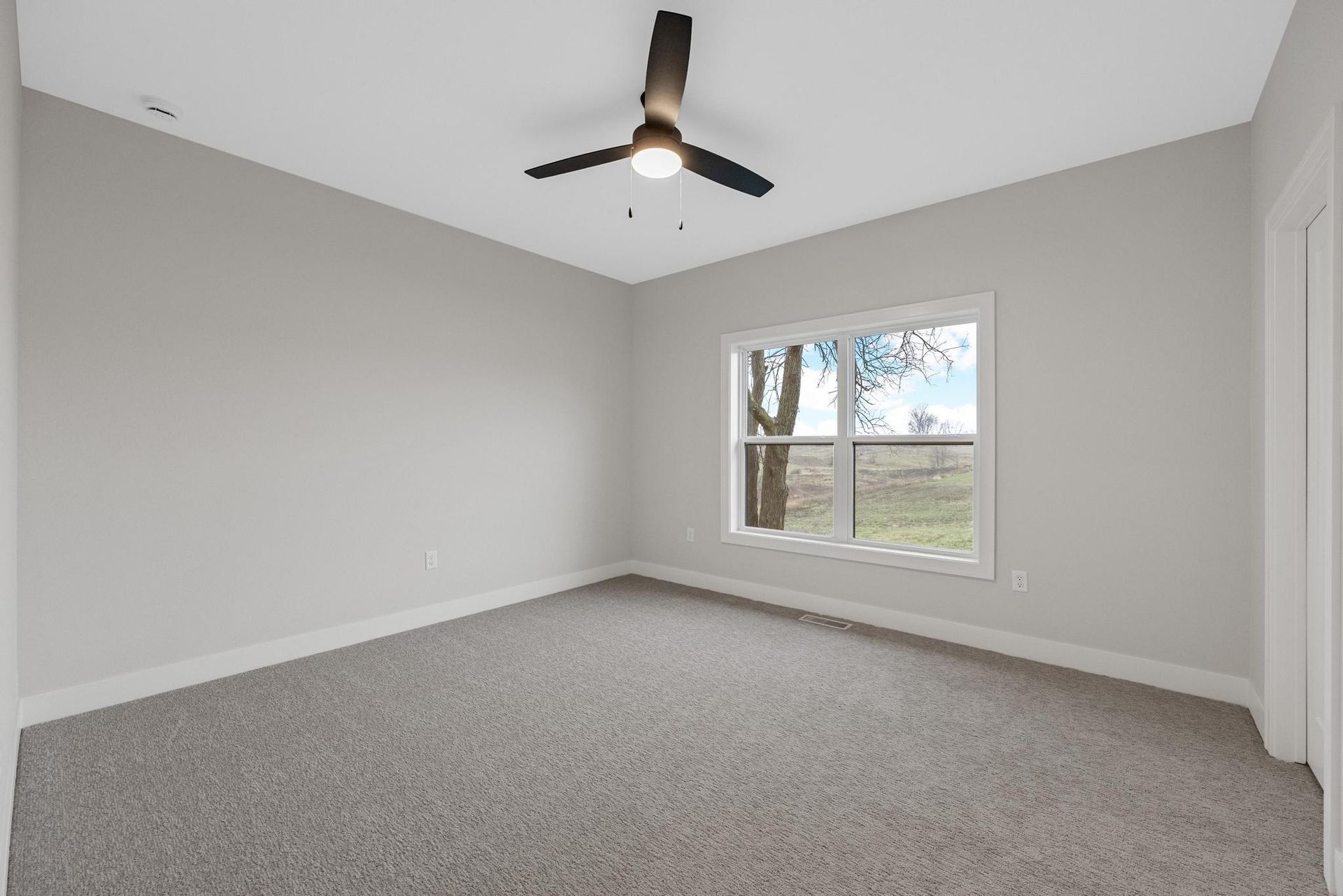 An empty bedroom with a ceiling fan and a window.
