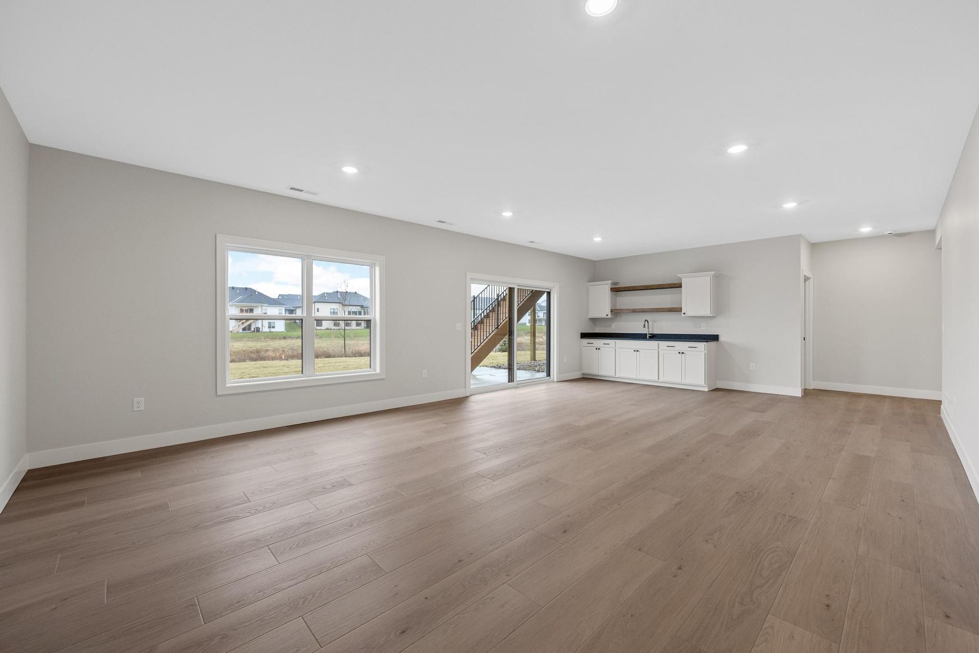 A large empty living room with hardwood floors and a kitchen.