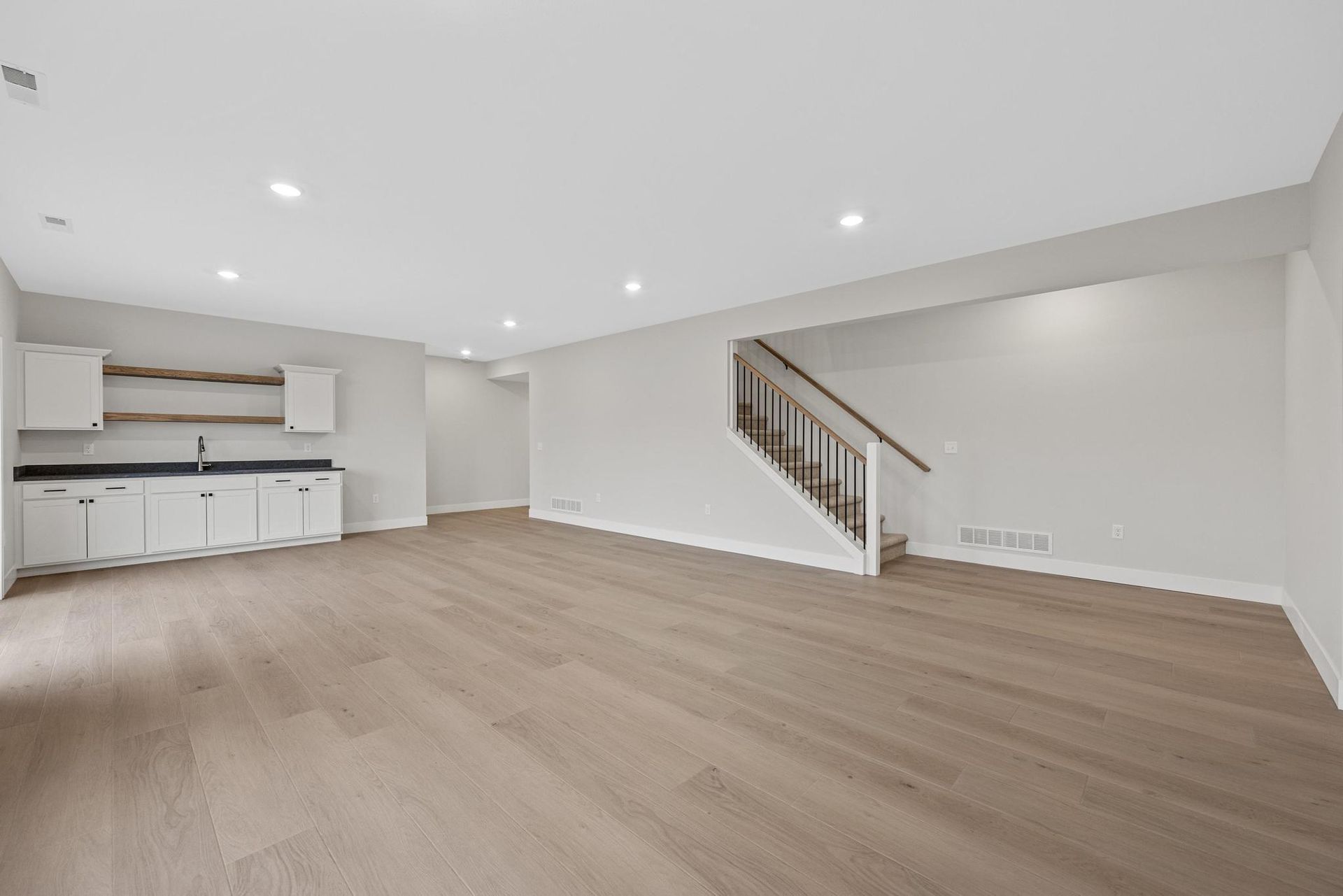 An empty basement with hardwood floors , white cabinets , and stairs.