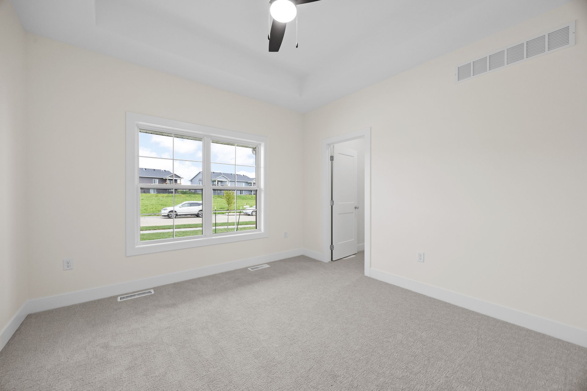 An empty bedroom with two windows and a ceiling fan.