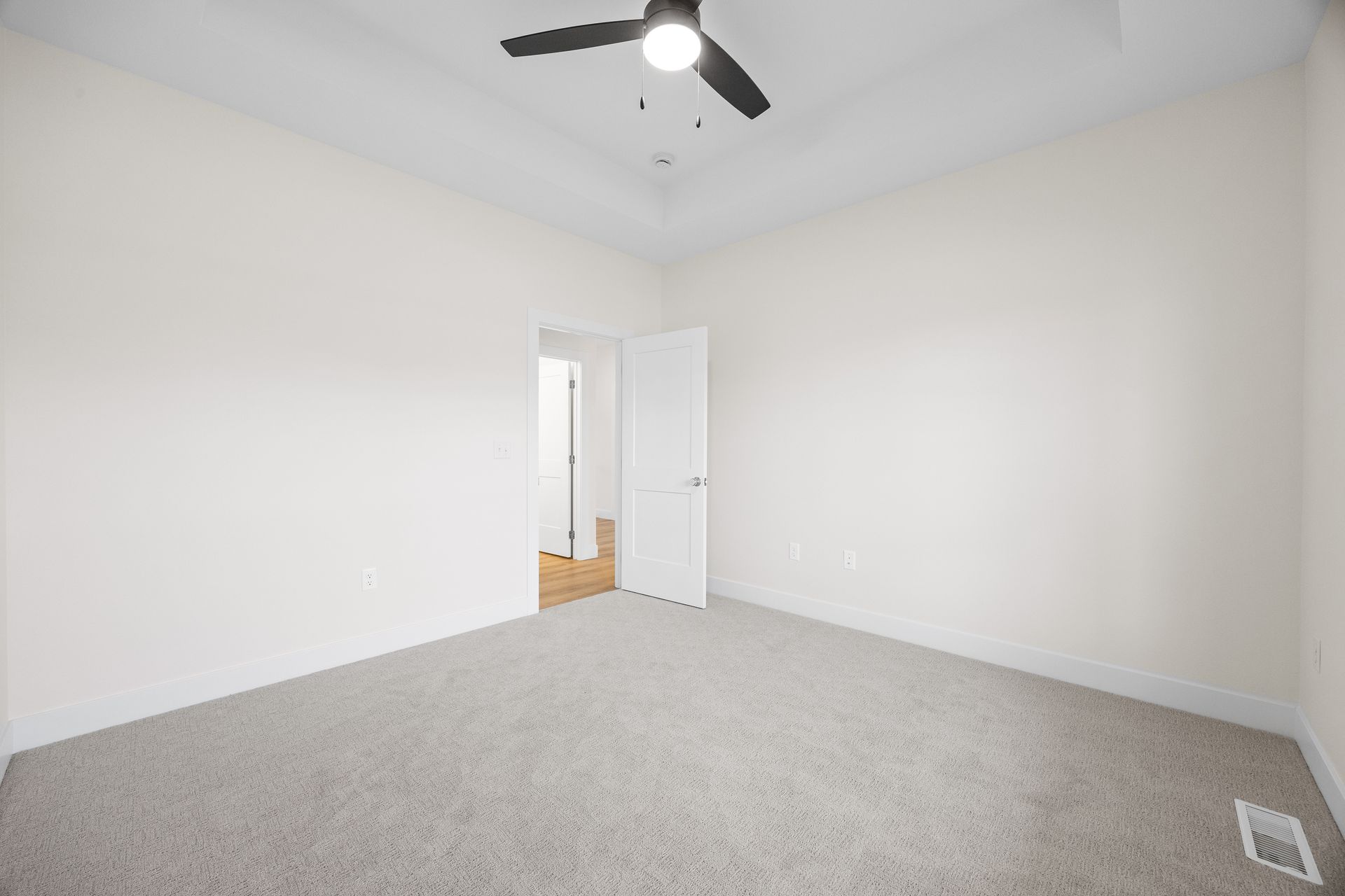 An empty bedroom with a ceiling fan and a door.