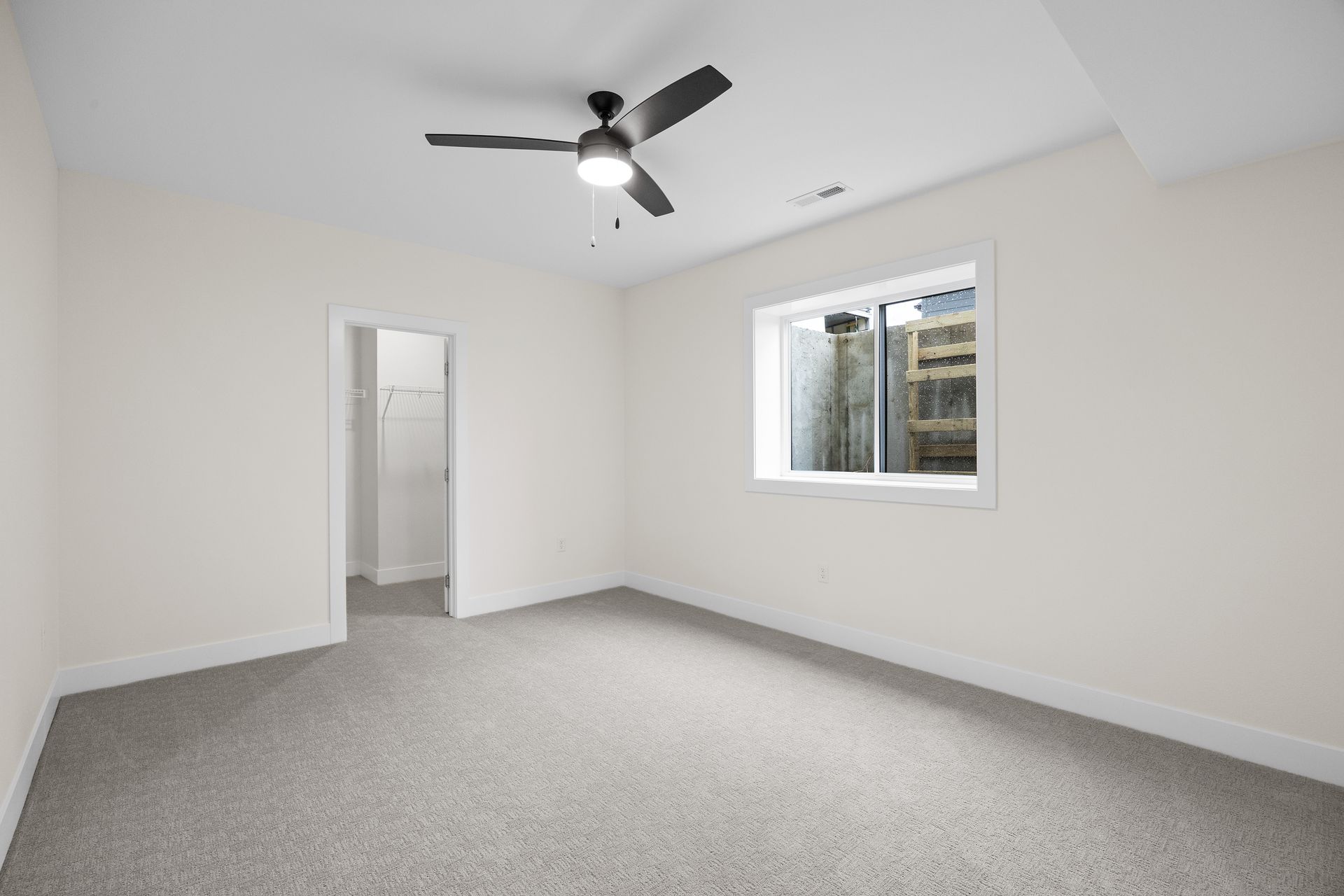 An empty bedroom with a ceiling fan and a window.